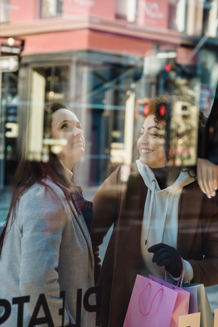 services-05 Through glass of positive female with packets standing near friend looking at mannequin at showcase of shop